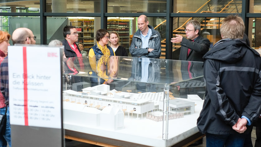 Personengruppe steht um ein Modell der Deutschen Nationalbibliothek in Frankfurt am Main, ein Gästeführer gibt Erläuterungen