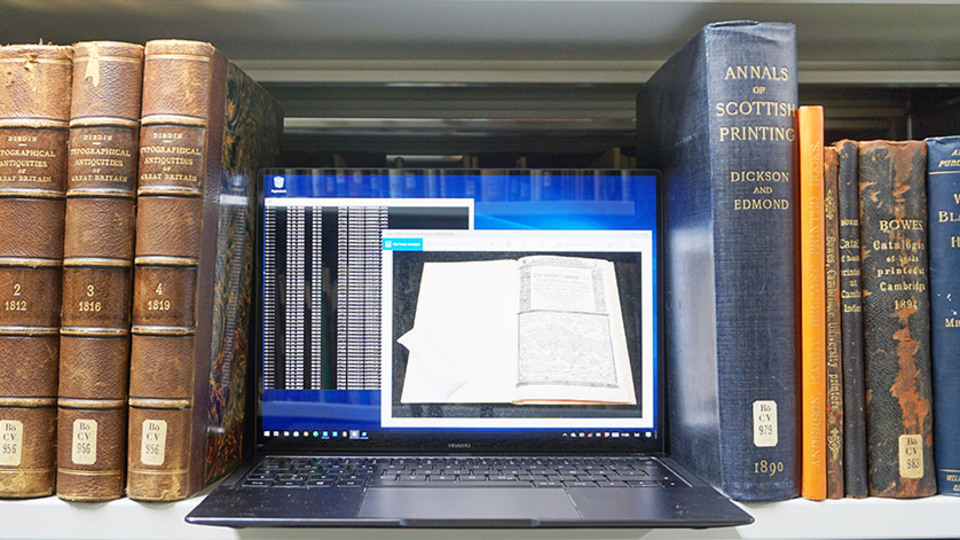 Eingeschaltetes Notebook und Bücher im Regal einer Bibliothek