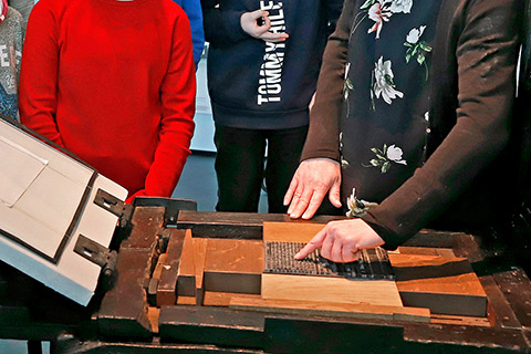 Eine Hand zeigt auf den in der Druckpresse arretierten Schriftsatz