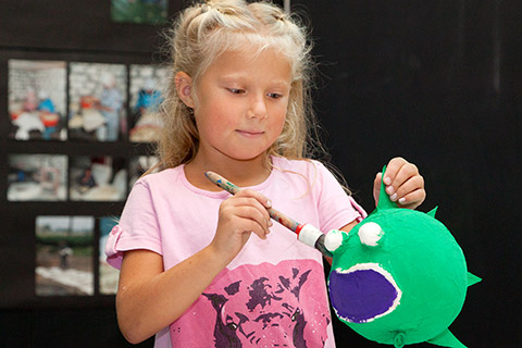 Ein Mädchen bestreicht einen Kugelfisch aus Pappmaché mit grüner Farbe
