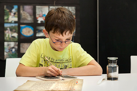 Ein Kind ritzt mit Griffel Schriftzeichen in Wachstafel