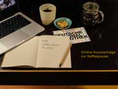 Tisch mit einem aufgeklappten Laptop, einem Kaffee und einemn Notizbuch, darauf steht „ DNB, Coffee Lectures, Mi, 15 Uhr“. 