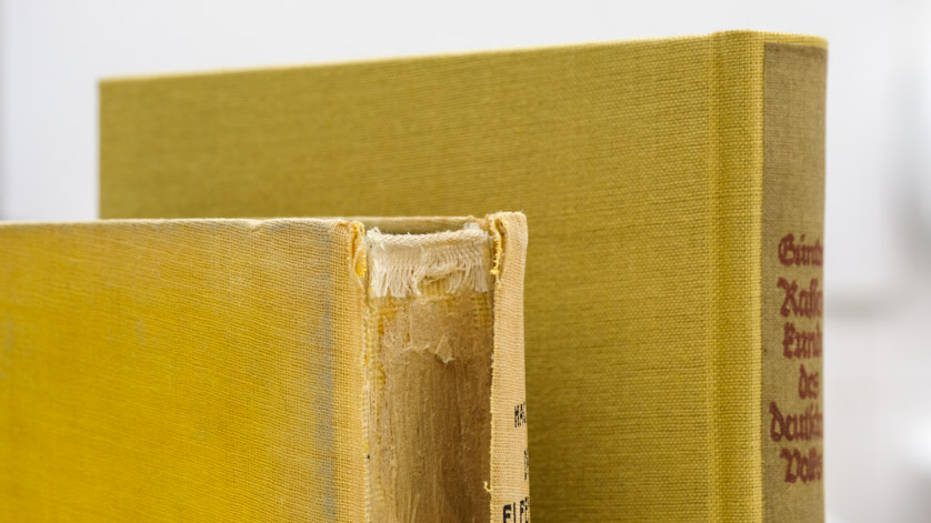 The badly damaged spine of a book in a before-and-after restoration comparison
